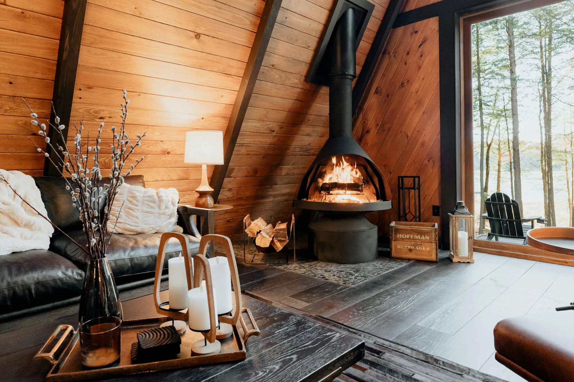 Wohnraum aus Holz mit brennendem Kaminofen, Kerzen und großem Fenster